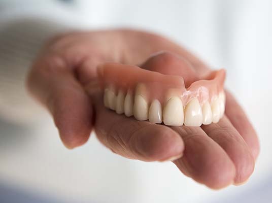 closeup of womans hand holding a teeth denture